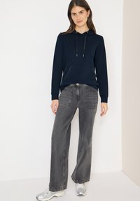 Granatowa bluza z kapturem z przednią kieszenią i sznurkami, zestawiona z luźnymi, szarymi dżinsami z naszywanymi kieszeniami i wyblakłą fakturą.