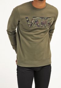 Sudadera verde oliva con logo "VANS" en camuflaje, cuello redondo y puños de canalé, confeccionada en tejido suave y de textura lisa.