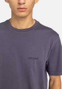 T-shirt di cotone viola con collo rotondo e maniche corte, dotata di un piccolo logo "element" nero sulla parte sinistra del petto.