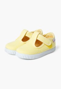 Scarpe di tela gialle con una fascia in velcro, punta rotonda e suola in gomma bianca. L'interno presenta un motivo a quadretti.
