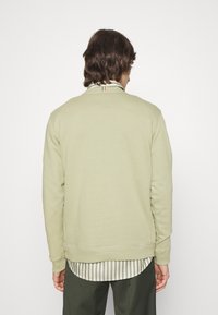 Jasnozielony sweatshirt z okrągłym dekoltem, długimi rękawami i ribbowymi mankietami, nałożony na pasekowy t-shirt z zaokrąglonym dołem.