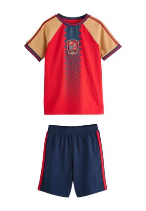 Rød og beige kortærmet skjorte med Spaniens emblem og blåt zigzag-mønster, kombineret med marineblå shorts med røde sidestreger.