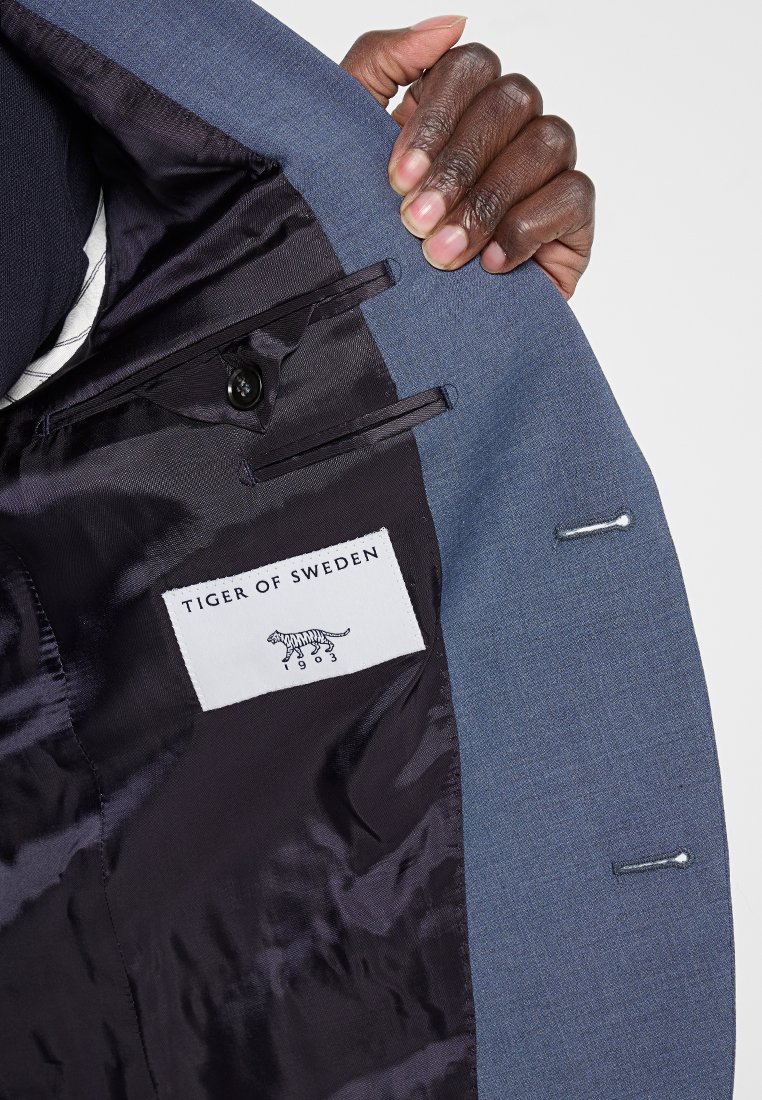 Das Innere des blauen Blazers verfügt über ein schwarzes Satinfutter, ein Etikett mit der Aufschrift "TIGER OF SWEDEN" und ein kleines gesticktes Tiger-Logo.