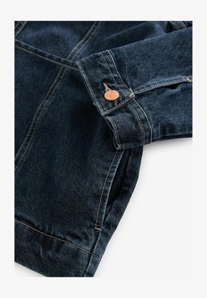 Tume teksajakk, millel on nupukinnitus, kontrastsed õmblused ja lõdvestatud sobivus. Kanga tekstuur on pehme ja pind sile.