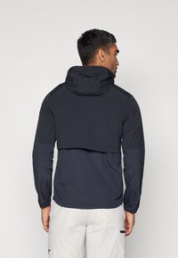 Black, lightweight jacket with a hood, featuring long sleeves and a cropped back design. Smooth texture, no visible patterns or hardware.
