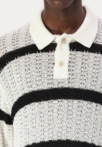 Knit pullover with lace in white and black horizontal stripes, featuring a soft white collar and three buttons at the neck. Textured fabric.