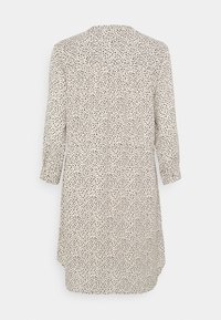Langärmliges Kleid aus einem hellen cremefarbenen Stoff mit einem schwarzen Punktmuster, mit einer Knopfleiste hinten und gerafften Details an der Taille.