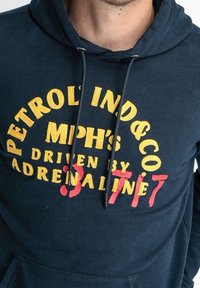 Granatowa bluza z kapturem z żółto-czerwonym haftowanym napisem. Napis zawiera słowa "PETROL IND & CO" oraz "ADRENALINE". Materiał to mieszanka bawełny.