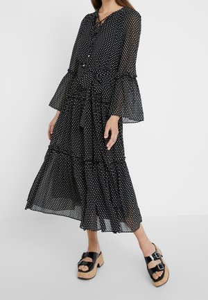 Femme portant une robe noire à manches longues à pois, avec des manches évasées et une jupe à volants, associée à des sandales plateforme noires à boucles.