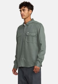 Groen langemouwshirt van zachte stof, met twee borstzakken, knoopsluiting en een klassieke kraagontwerp.