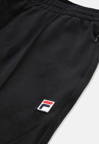 Svarta sweatpants i mjukt material, med ett elastiskt midjeband och en liten broderad logotyp i rött, vitt och blått.