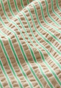 Texturerad tyg som har alternerande beige och gröna vertikala ränder, med ett subtilt mönster som ger en vågig känsla.