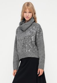 Grå strikket genser med design av cowl-hals. Har sølvfargede paljetter ordnet i vertikale striper. Myk tekstur, cropped lengde.