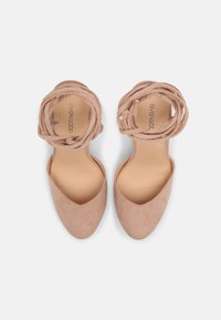 Nude pink high-heeled shoes with a smooth suede finish and braided ankle straps, featuring a pointed toe design and a flat sole.