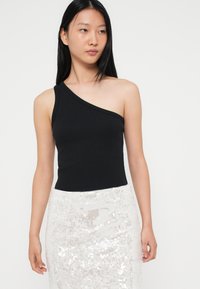 Black one-shoulder top made of ribbed fabric paired with a white, sequined, knee-length skirt, featuring smooth texture and fitted design.