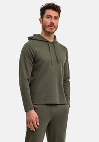 Felpa verde oliva in tessuto a costine con cappuccio regolabile, maniche lunghe e vestibilità ampia, abbinata a pantaloni coordinati.