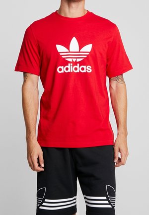 Rotes Baumwoll-T-Shirt mit kurzen Ärmeln, versehen mit einem großen weißen Adidas-Logo und dem ikonischen Drei-Streifen-Design. Kombiniert mit schwarzen Shorts.