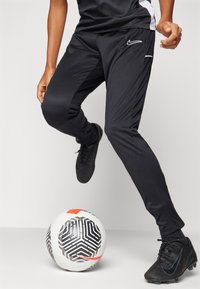 Sorte treningbukser med strømlinjeformet passform, hvite sideaksenter, kombinert med sorte fotballsko. En mønstret fotball ligger i nærheten.
