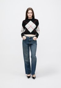 Camisola curta de losangos em preto, cinza e branco com detalhes em vermelho, combinada com jeans de ganga azul cintura alta e saltos pretos de bico fino.