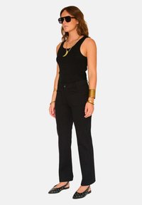 Débardeur noir et pantalon ajusté, bijoux en or superposés, lunettes de soleil noires surdimensionnées et ballerines pointues avec découpes circulaires.