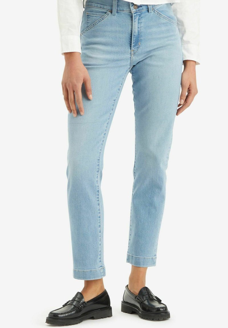 Hellblaue Denim-Jeans mit geradem Bein, hoher Taille, frontalen Taschen und einer dezenten, verblassten Textur. Tragen mit schwarzen Slippern.