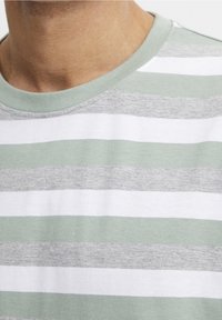 Camiseta a rayas con bandas alternas de gris claro, blanco y verde pálido. Fabricada con un tejido suave y con un escote redondeado.