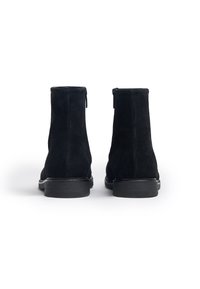 Bottines en cuir suede noir avec une texture lisse, à bouts ronds et semelles en caoutchouc noir contrastant. Comprend une fermeture éclair sur le côté.