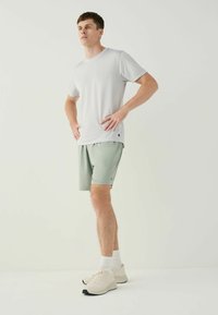 Light grey textured t-shirt paired with light green shorts. Model stands with hands on hips, wearing beige sneakers and white socks.