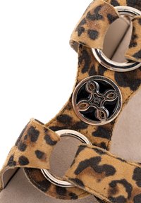 Sandalrem med leopardmønster, prydet med sølvfarvede ringe og et dekorativt metalemblem i sort og sølv.