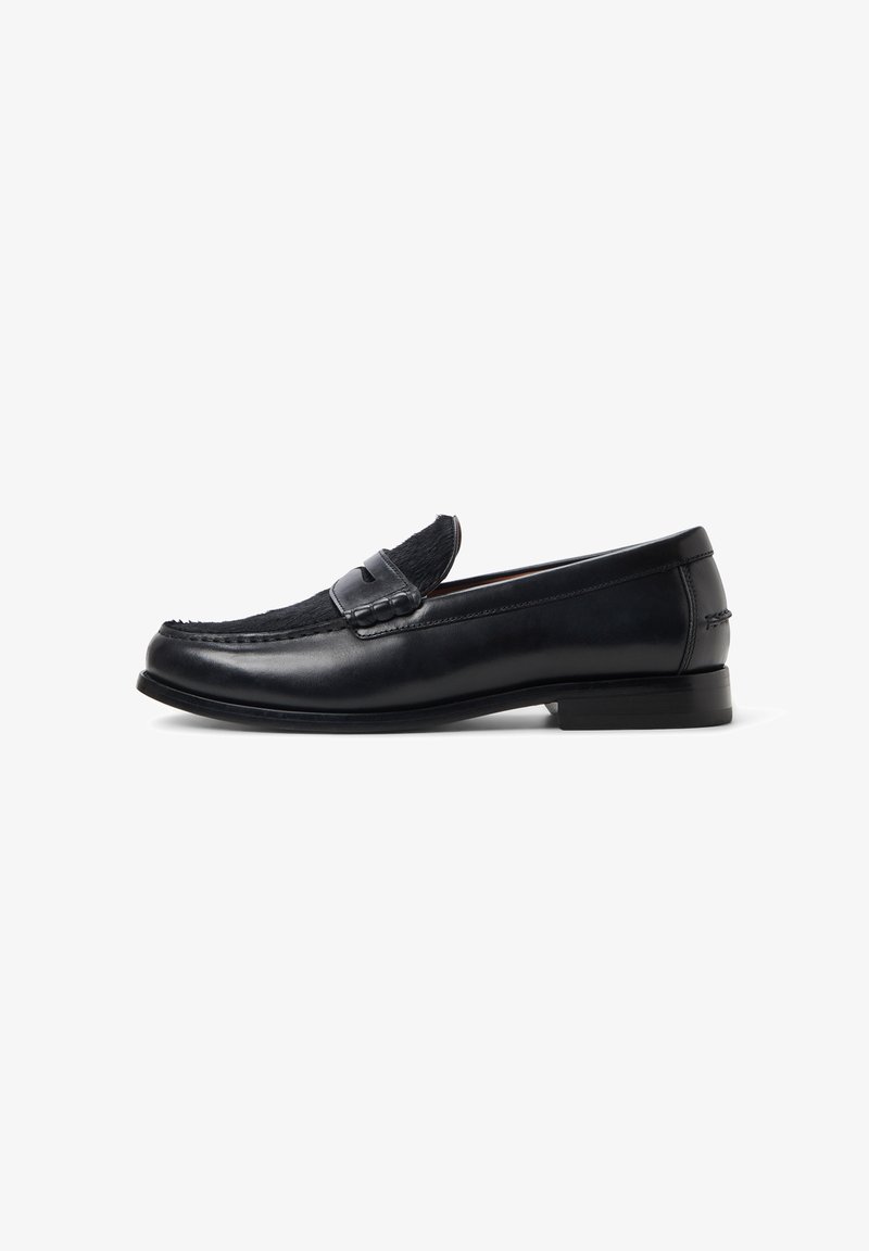 Mocassin en cuir noir avec une partie supérieure texturée en fourrure et un petit talon empilé, présenté en profil latéral sur un fond blanc.