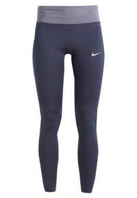 Granatowe legginsy sportowe sięgające do kostek z szerokim jasnoszarym pasem w talii i małym białym logo Nike na górnej części uda.