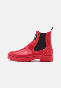 Bottes Chelsea en caoutchouc rouge avec une finition brillante, des panneaux latéraux élastiques et une semelle robuste pour une bonne adhérence. Dispose d'une languette arrière pour un enfilage facile.