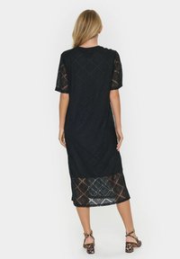 Black lace dress featuring a diamond pattern, short sleeves, and a semi-sheer bottom. Worn with animal print block-heeled sandals.