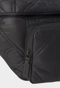 Gequilted zwarte stoffen tas met een ritszak met een zwarte trekband en Calvin Klein branding. Gladde textuur met subtiele patroondetails.