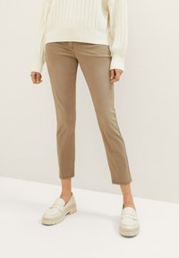 Pantalons beige à coupe ajustée avec une texture lisse, ourlet court et style décontracté, associés à des mocassins de couleur claire et un pull en maille côtelée blanc.
