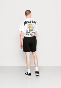White t-shirt with graphic print featuring a smiling face and text, paired with black shorts. Black sneakers with white soles and socks.