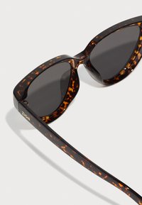 Tortoiseshell sunglasses with gray lenses, angular frames, and a glossy finish, featuring a gold logo on the temple.