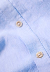 Ljusblå skjorta i linneblandning med synlig textur, två knappar med en naturlig finish och en prydlig knappslådesign.