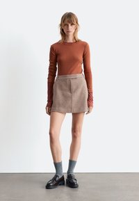 Brauner gerippter Langarmtop kombiniert mit einem hellbraunen strukturierten Minirock, ergänzt durch dunkle Slipper und graue Socken. Einfaches Design.