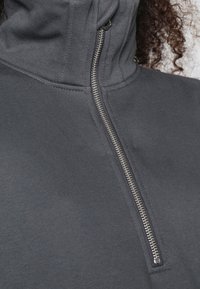 Sweat-shirt gris à fermeture éclair avec un col montant, doté d'une fermeture éclair métallique sur le devant et d'un tissu doux et texturé.