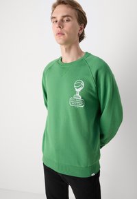 Grön sweatshirt med långa ärmar, ribbat avslut och rund hals. Har en vit grafik av en baskettrofé och text på framsidan.