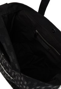 Sac fourre-tout noir en tissu robuste, présentant un motif géométrique, une poche zippée intérieure et une doublure lisse et texturée.