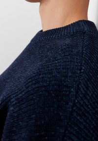 Suéter de punto azul marino con cuello redondo acanalado, patrones texturizados y un diseño ajustado. Tela suave visible en el primer plano.