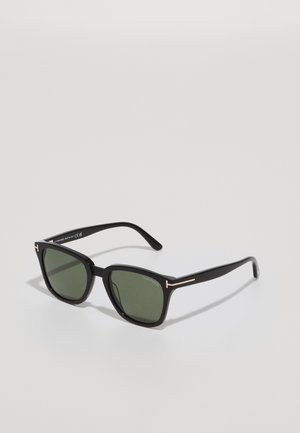 Gafas de sol negras con montura geométrica, lentes verde oscuro, acentos metálicos en las varillas y acabado mate texturizado.