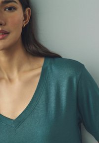 T-shirt vert canard en V fabriqué en tissu doux, avec une coupe décontractée et des manches courtes, présentant des coutures visibles et une texture lisse.