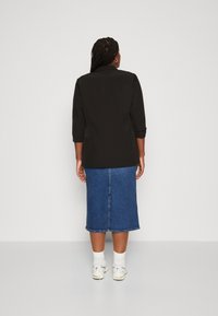 Black tailored blazer with three-quarter sleeves, paired with a denim skirt. The skirt is knee-length with a straight cut and back slit.