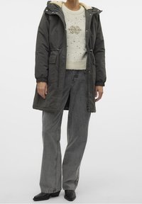 Prošívaná parka tmavě zelené barvy s kapucí lemovanou umělou kožešinou, dvě boční kapsy, doplněno lehkým svetrem a šedými džínami s širokými nohavicemi.