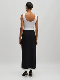 Witte geribde tanktop gecombineerd met een lange zwarte rok met een crèmekleurige zoom, afgewerkt met zwarte hakken en doorschijnende zwarte panty's.