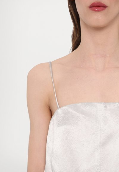 Sølv sateng cami med delikate spaghetti-stropper og en lett teksturert finish, med synlige sømmer langs halslinjen og kanten.