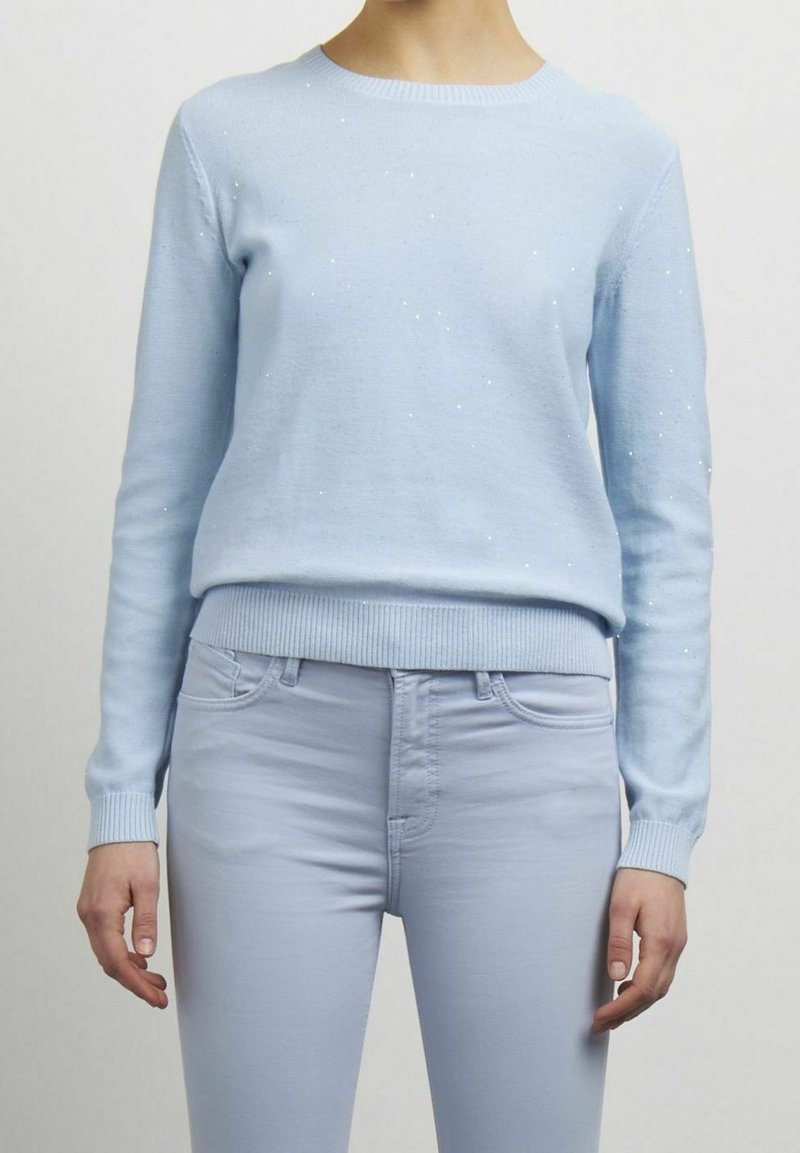 Helles blaues Sweatshirt aus weichem Material, mit langen Ärmeln, runden Halsausschnitt und verstreuten Pailletten für Textur; kombiniert mit passenden Skinny-Jeans.